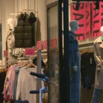Etalage van een kledingwinkel met grote uitverkoopborden en paspoppen.