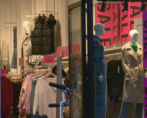 Etalage van een kledingwinkel met grote uitverkoopborden en paspoppen.