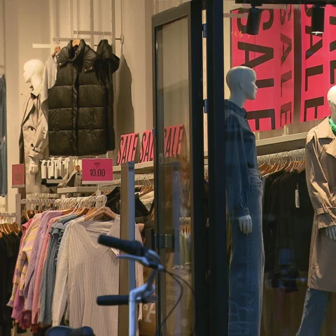 Etalage van een kledingwinkel met grote uitverkoopborden en paspoppen.