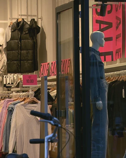 Etalage van een kledingwinkel met grote uitverkoopborden en paspoppen.