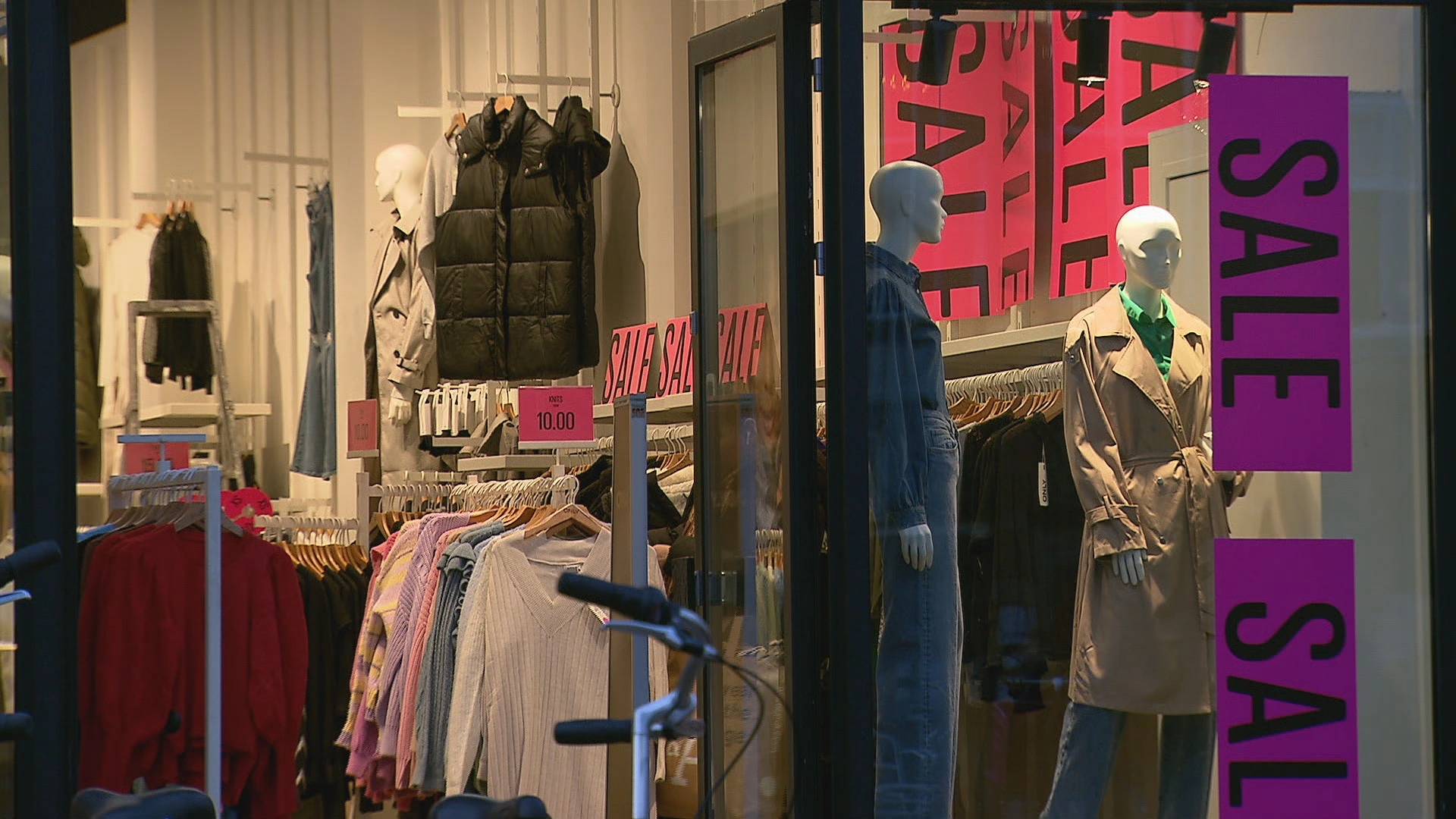 Etalage van een kledingwinkel met grote uitverkoopborden en paspoppen.