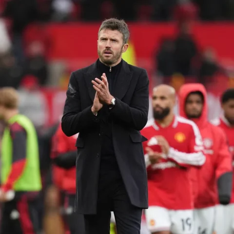 Michael Carrick staat langs de zijlijn terwijl Manchester United-spelers op de achtergrond applaudisseren.