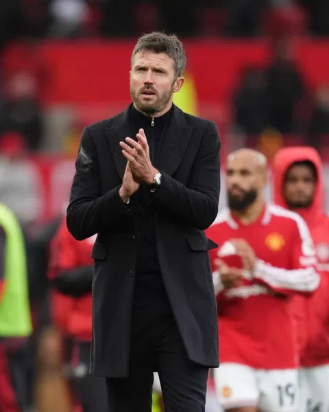Michael Carrick staat langs de zijlijn terwijl Manchester United-spelers op de achtergrond applaudisseren.