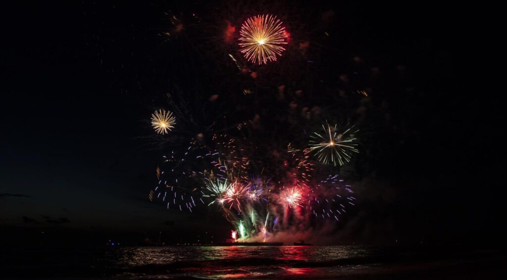 Vuurwerk explodeert boven water in de nachtelijke hemel.