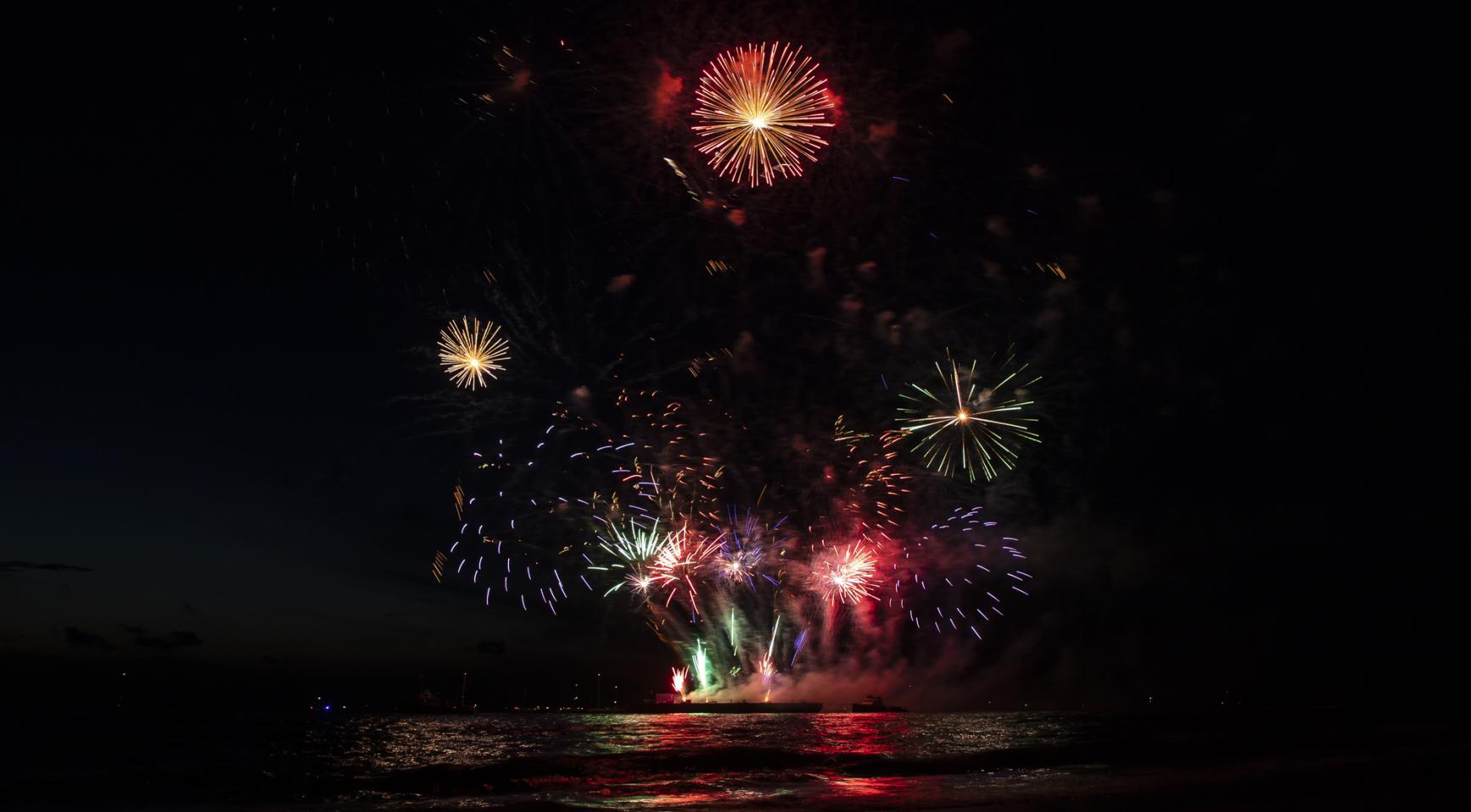 Vuurwerk explodeert boven water in de nachtelijke hemel.