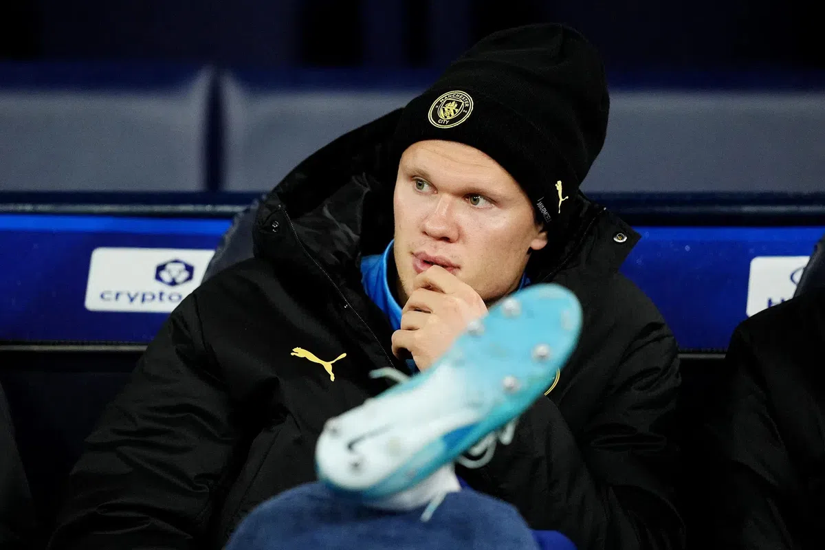 Manchester City-speler zit op de bank in clubkleding en muts.
