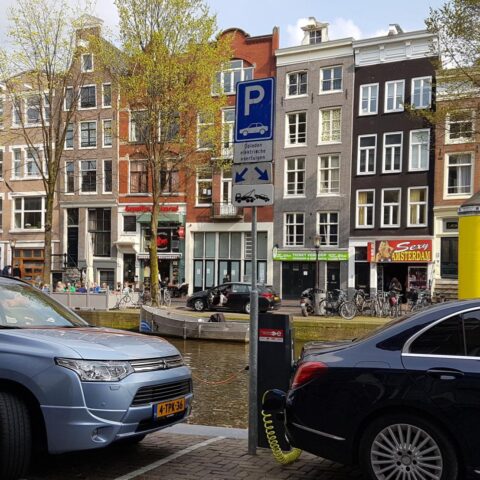Geparkeerde auto's langs een Amsterdamse gracht met een parkeersignaal op straat.
