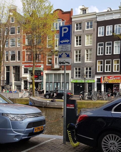 Geparkeerde auto's langs een Amsterdamse gracht met een parkeersignaal op straat.