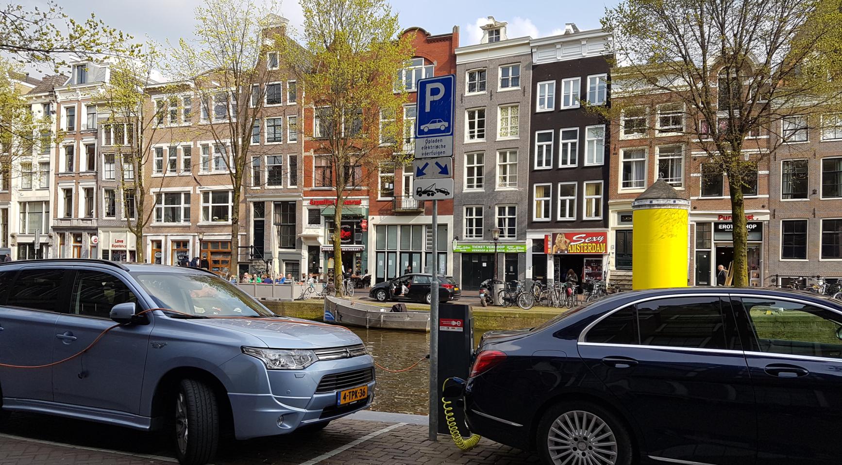 Geparkeerde auto's langs een Amsterdamse gracht met een parkeersignaal op straat.