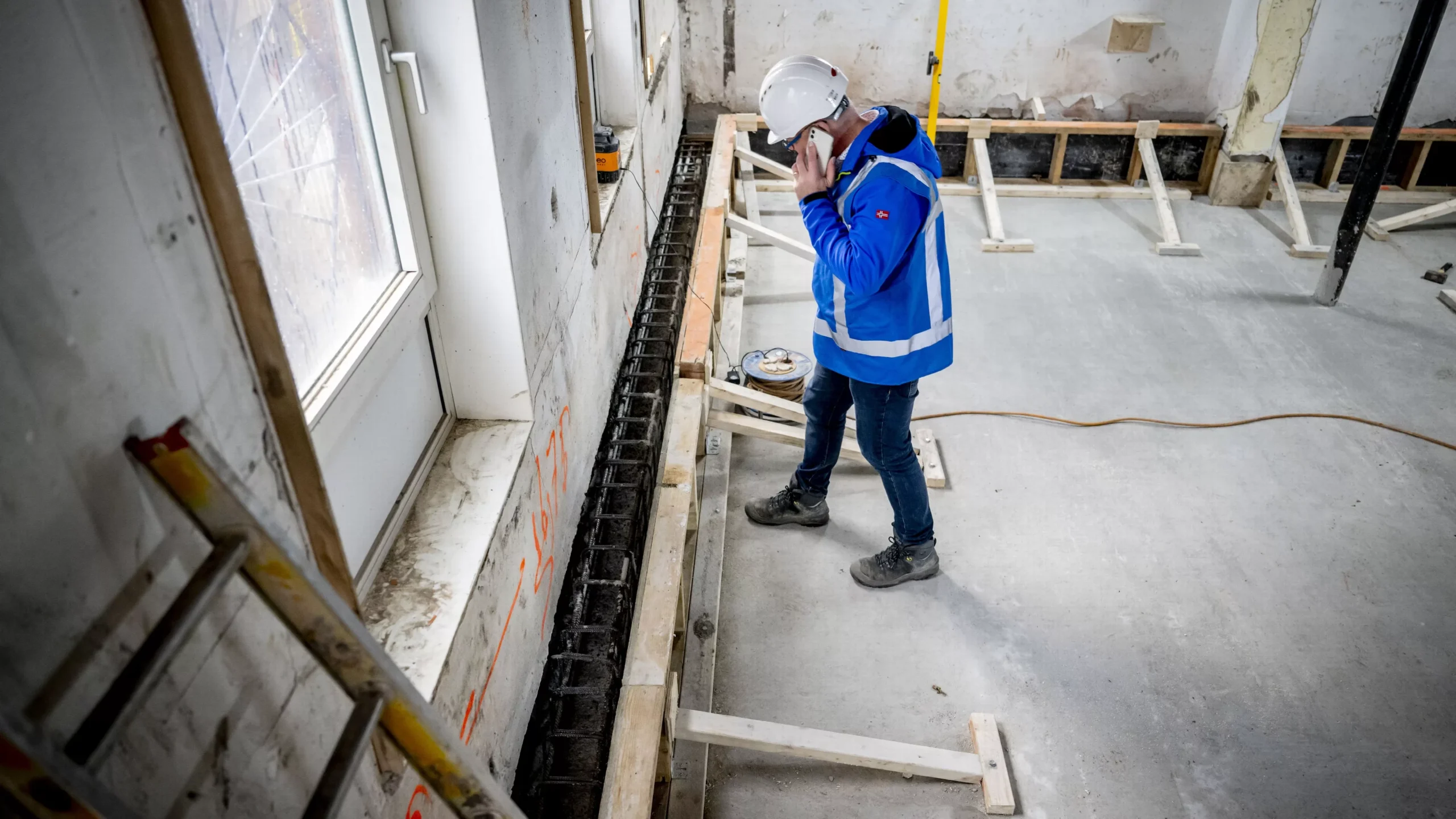 Een bouwmedewerker in beschermende kleding inspecteert funderingsherstel in een gebouw.