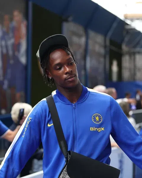 Een Chelsea-speler in blauwe trainingskleding loopt buiten het stadion.