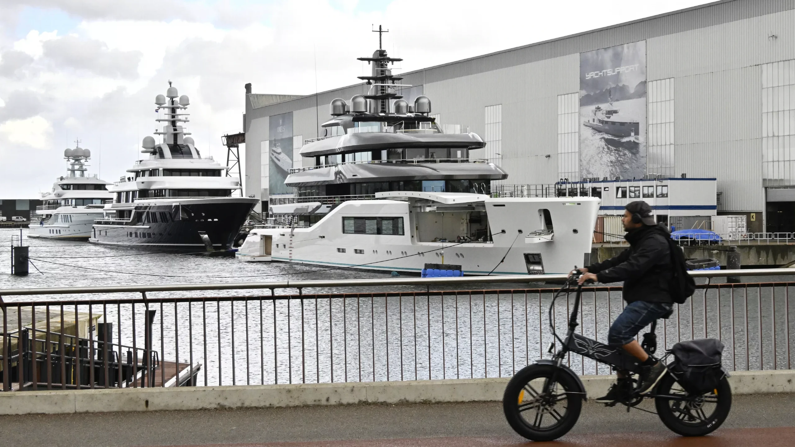 Jachten liggen bij een scheepswerf van Damen, met grote werfgebouwen op de achtergrond.