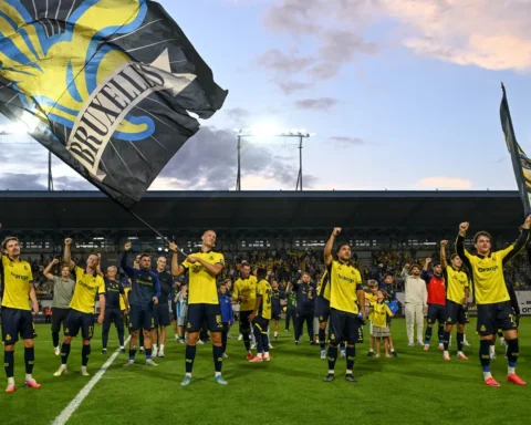 Union Saint-Gilloise spelers en supporters op het veld na een wedstrijd, met grote clubvlaggen in het stadion.