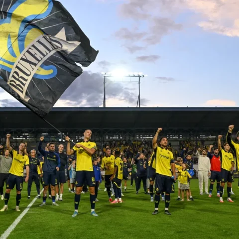 Union Saint-Gilloise spelers en supporters op het veld na een wedstrijd, met grote clubvlaggen in het stadion.