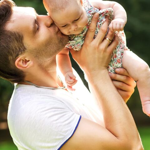 Man houdt een baby vast en kust haar buiten in een park.