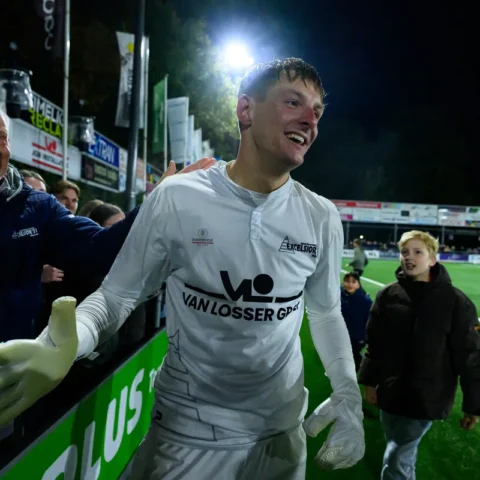 Kevin Reimink in een wit keepershirt na de wedstrijd, lachend langs het veld terwijl supporters hem feliciteren.