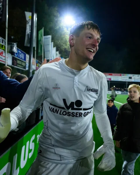 Kevin Reimink in een wit keepershirt na de wedstrijd, lachend langs het veld terwijl supporters hem feliciteren.