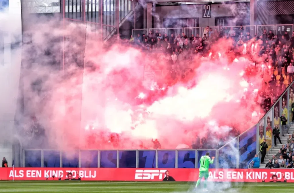 Rode rook van fakkels stijgt op in een voetbalstadion tijdens een wedstrijd.