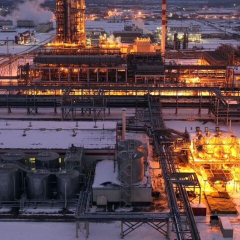 Verlichte olie- of raffinaderij-installatie in een besneeuwd industrieel complex bij schemering.