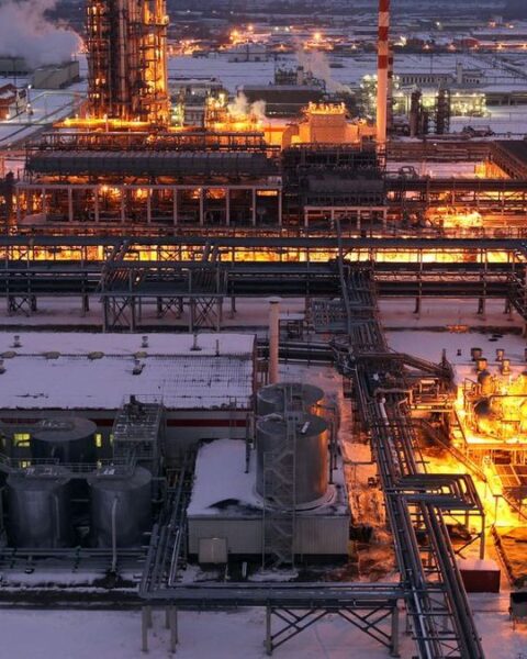 Verlichte olie- of raffinaderij-installatie in een besneeuwd industrieel complex bij schemering.