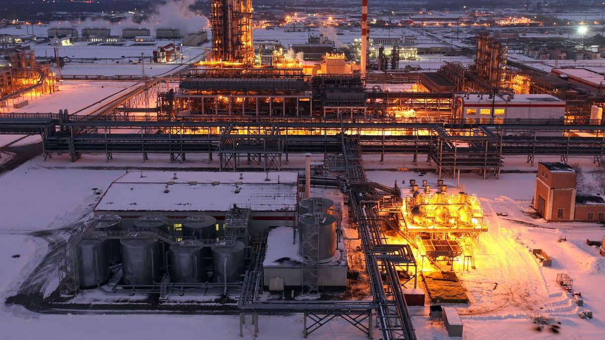 Verlichte olie- of raffinaderij-installatie in een besneeuwd industrieel complex bij schemering.