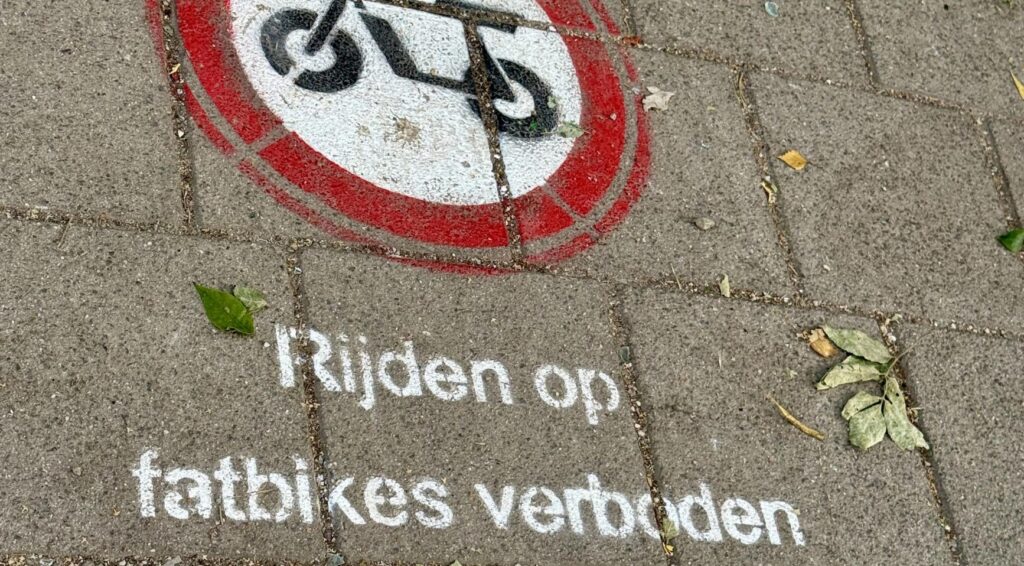Op de stoep staat een rood-wit verbodspictogram voor fatbikes met de tekst ‘Rijden op fatbikes verboden’.