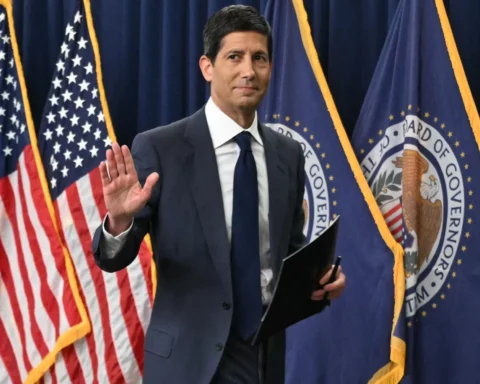 Man in pak staat voor Amerikaanse en Federal Reserve-vlaggen en steekt een hand op.