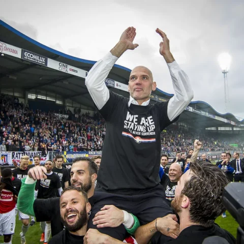 Jurgen Streppel wordt op het veld in een stadion gejuicht terwijl hij zijn armen omhoog steekt.