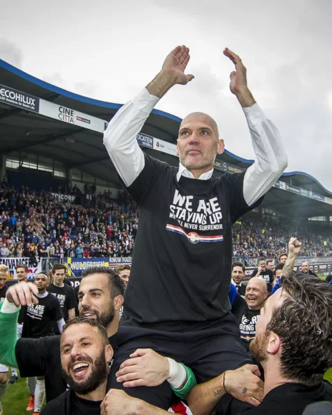 Jurgen Streppel wordt op het veld in een stadion gejuicht terwijl hij zijn armen omhoog steekt.
