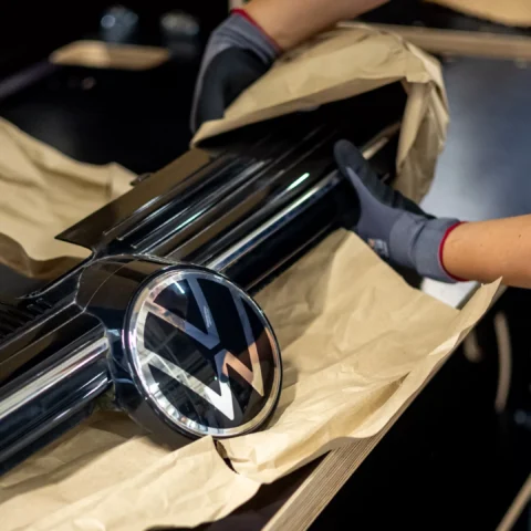 Werknemer verpakt een Volkswagen-grille met het VW-logo in een werkplaats.