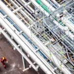 Luchtfoto van grote industriële pijpleidingen met twee werknemers in beschermende kleding eronder.