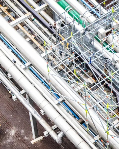 Luchtfoto van grote industriële pijpleidingen met twee werknemers in beschermende kleding eronder.