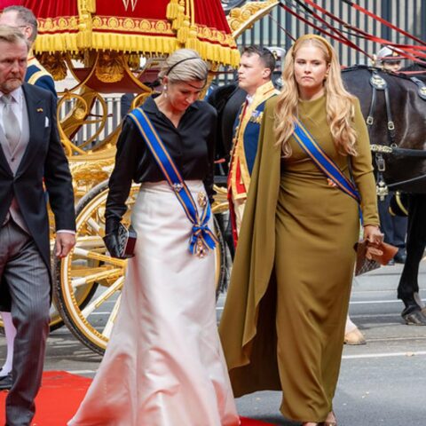 Leden van het Nederlandse koningshuis lopen langs een gouden koets en paarden tijdens een ceremonieel moment.