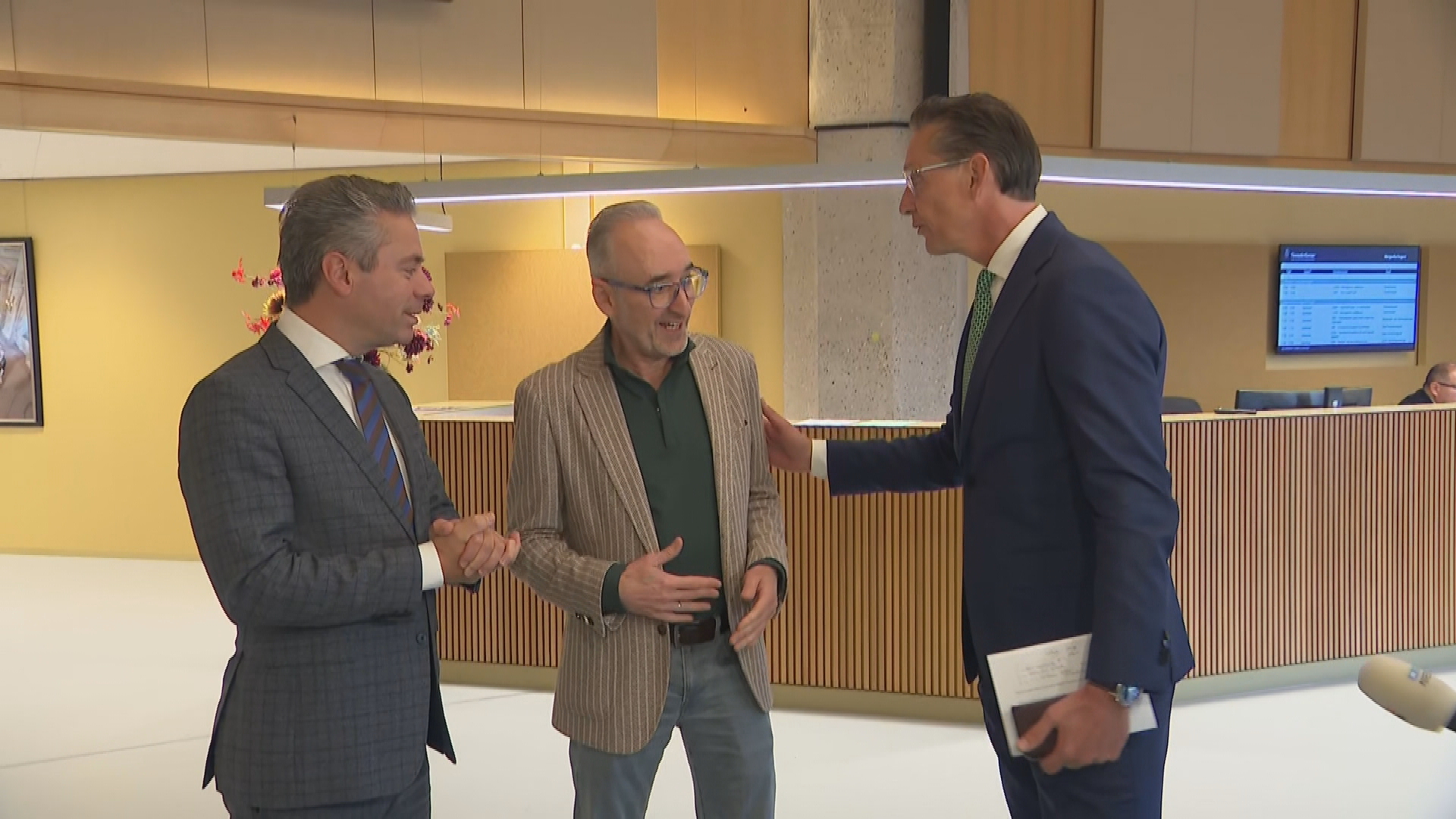 Drie mannen staan met elkaar te praten in een overheidsgebouw.