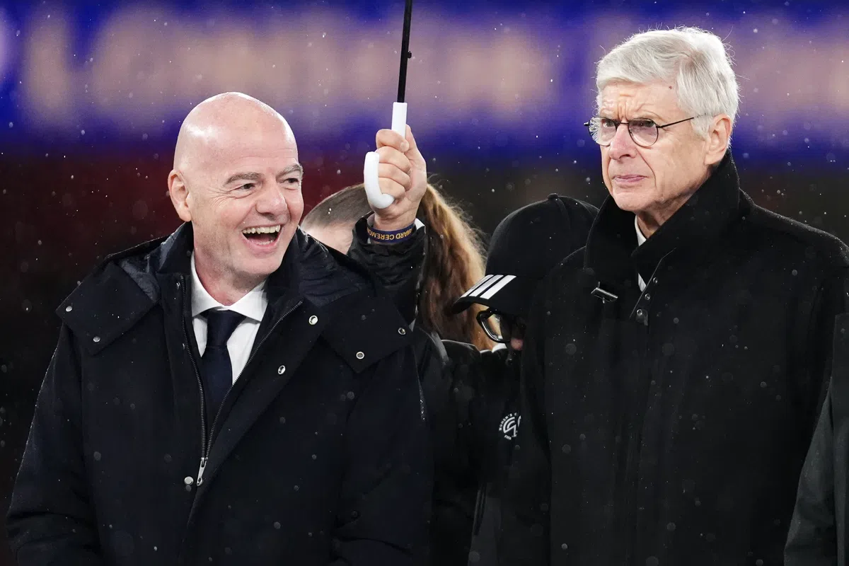 Gianni Infantino en Arsène Wenger staan naast elkaar in een stadion tijdens regenachtig weer.