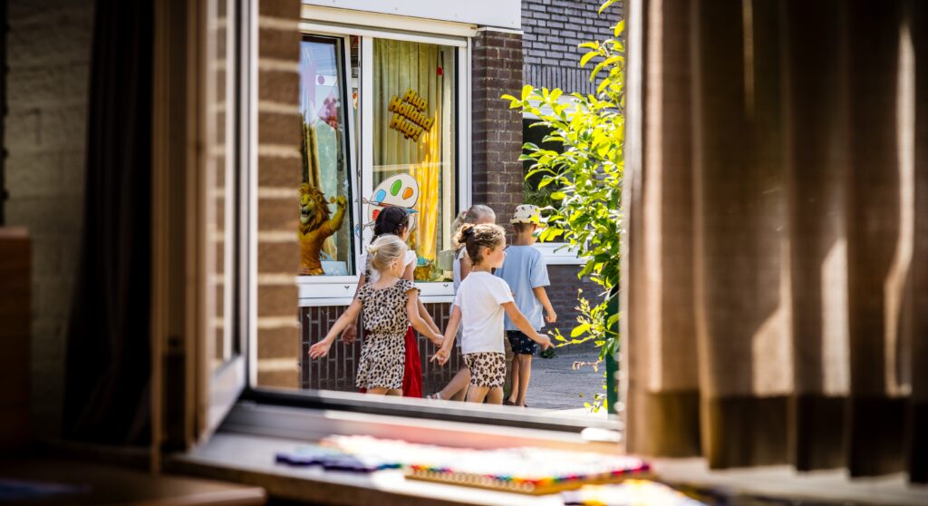 Kinderen lopen langs een gebouw met een versierde raamruit.