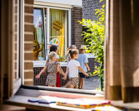 Kinderen lopen langs een gebouw met een versierde raamruit.