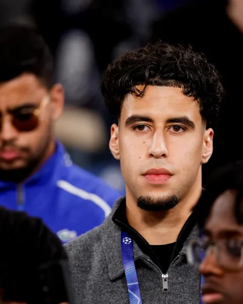 Een jonge man staat tussen andere toeschouwers of teamleden.