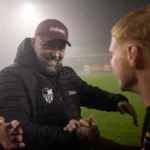 Theo Janssen schudt handen met spelers langs het veld in een mistig stadion.