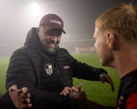 Theo Janssen schudt handen met spelers langs het veld in een mistig stadion.
