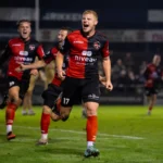 De Treffers-spelers vieren een doelpunt op het veld tijdens een avondwedstrijd.