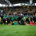 Voetballers van een team vieren met supporters in een stadion na een wedstrijd.