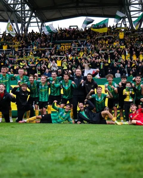 Voetballers van een team vieren met supporters in een stadion na een wedstrijd.