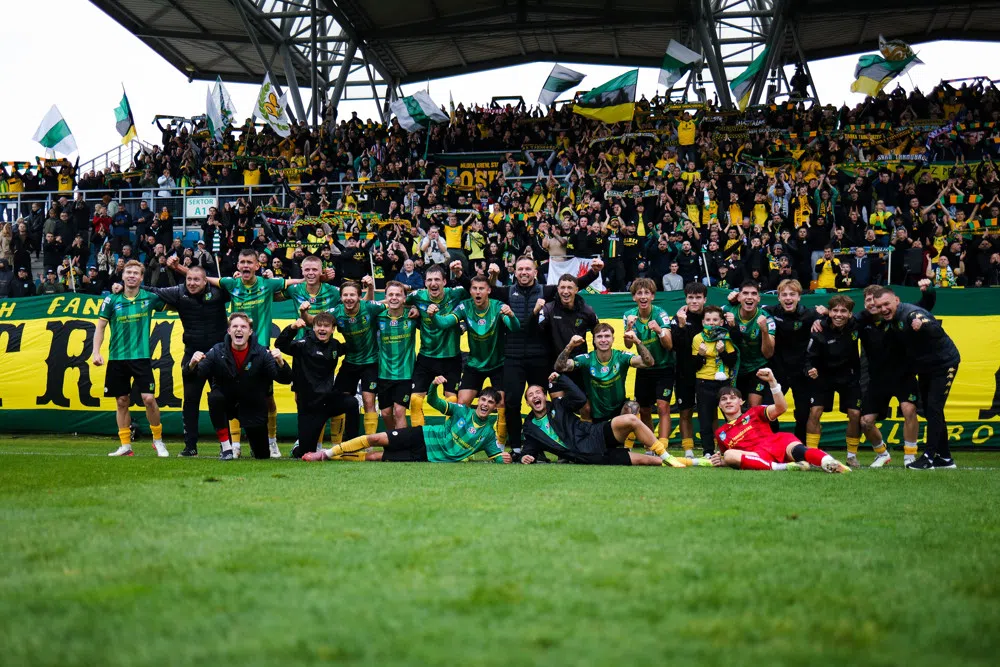 Voetballers van een team vieren met supporters in een stadion na een wedstrijd.