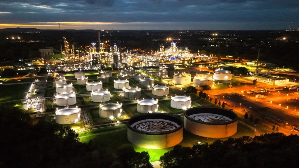 Luchtfoto van een olie- en raffinaderijcomplex met meerdere opslagtanks, 's nachts verlicht.