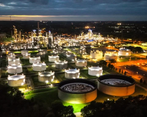 Luchtfoto van een olie- en raffinaderijcomplex met meerdere opslagtanks, 's nachts verlicht.