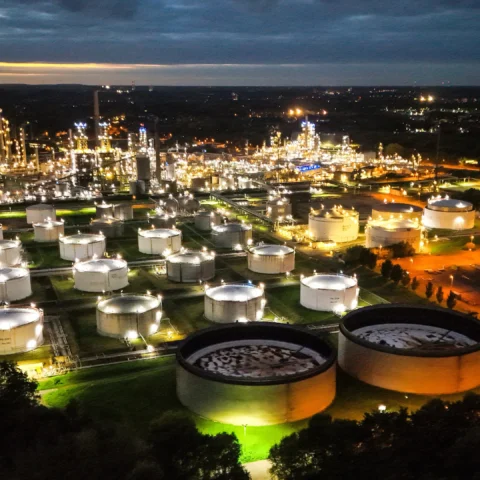 Luchtfoto van een olie- en raffinaderijcomplex met meerdere opslagtanks, 's nachts verlicht.