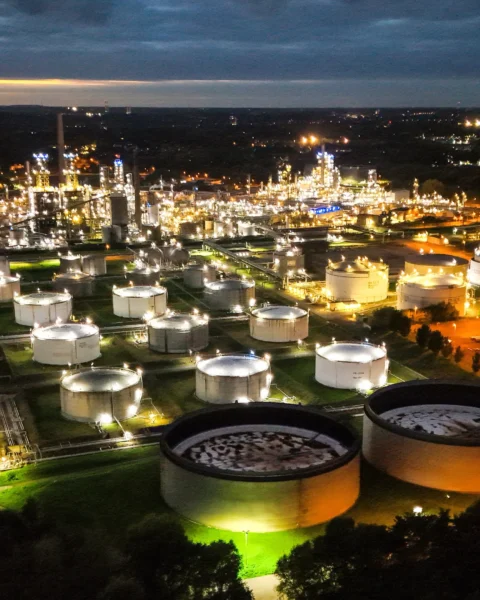 Luchtfoto van een olie- en raffinaderijcomplex met meerdere opslagtanks, 's nachts verlicht.