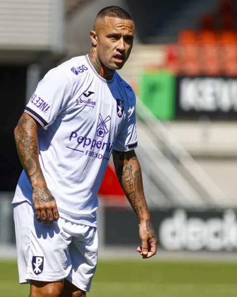 Radja Nainggolan staat in een wit voetbalshirt op het veld.