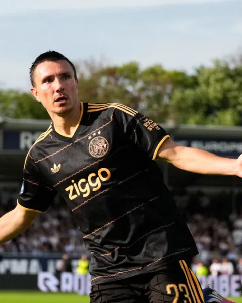Ajax-speler in zwart uittenue juicht op het veld tijdens een wedstrijd.